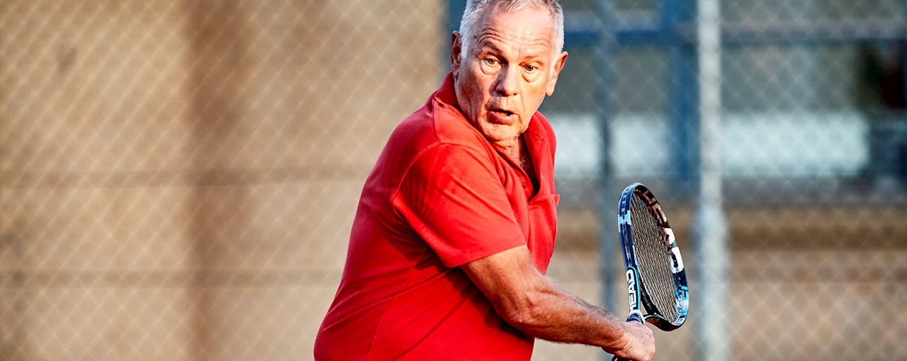 Ældre tennismand slår enkeltbaghånd